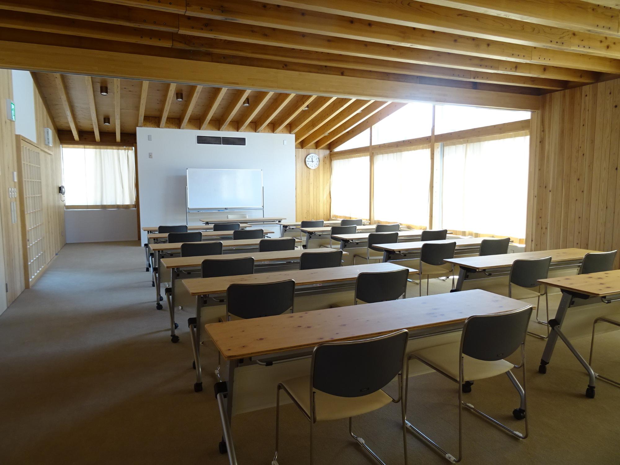 木製の机が並んでいる人のいない大会議室の写真