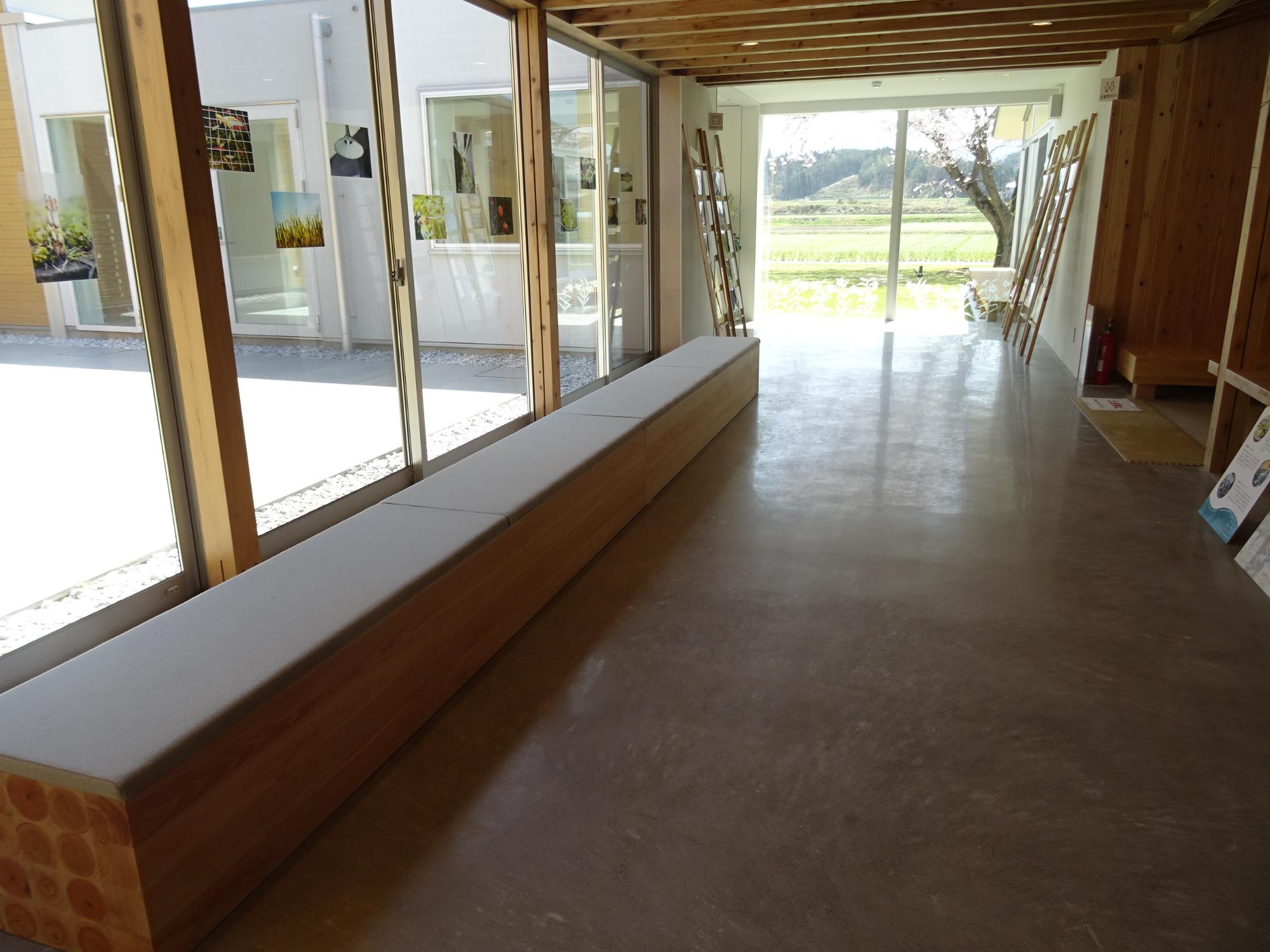 ガラス張りの窓沿いにベンチが設けられた明るい通路を奥まで写した写真