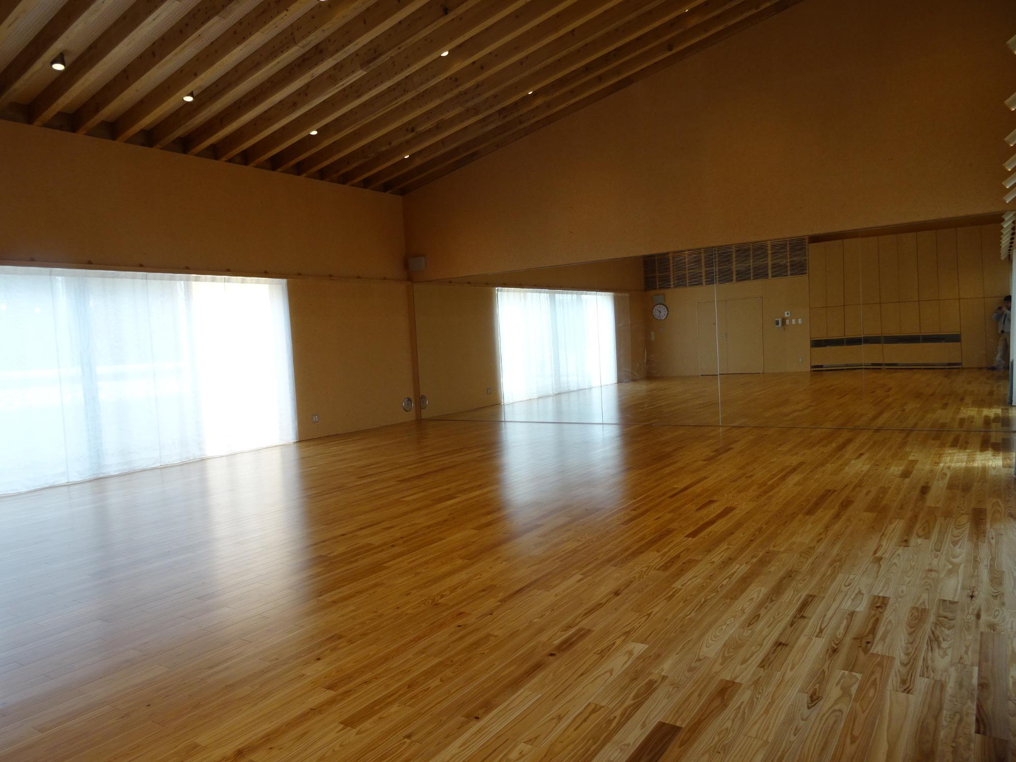 木の梁が見える天井と広い床面が特徴の何も置かれていない多目的室の全体を写した写真