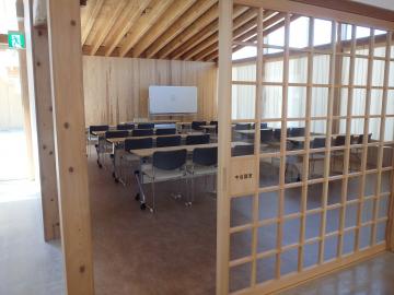 木製の格子戸越しに机と椅子が並ぶ会議室全体を写した写真