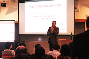 講堂で男性講師がマイクを持って講演しているのを来場者が聞いている写真