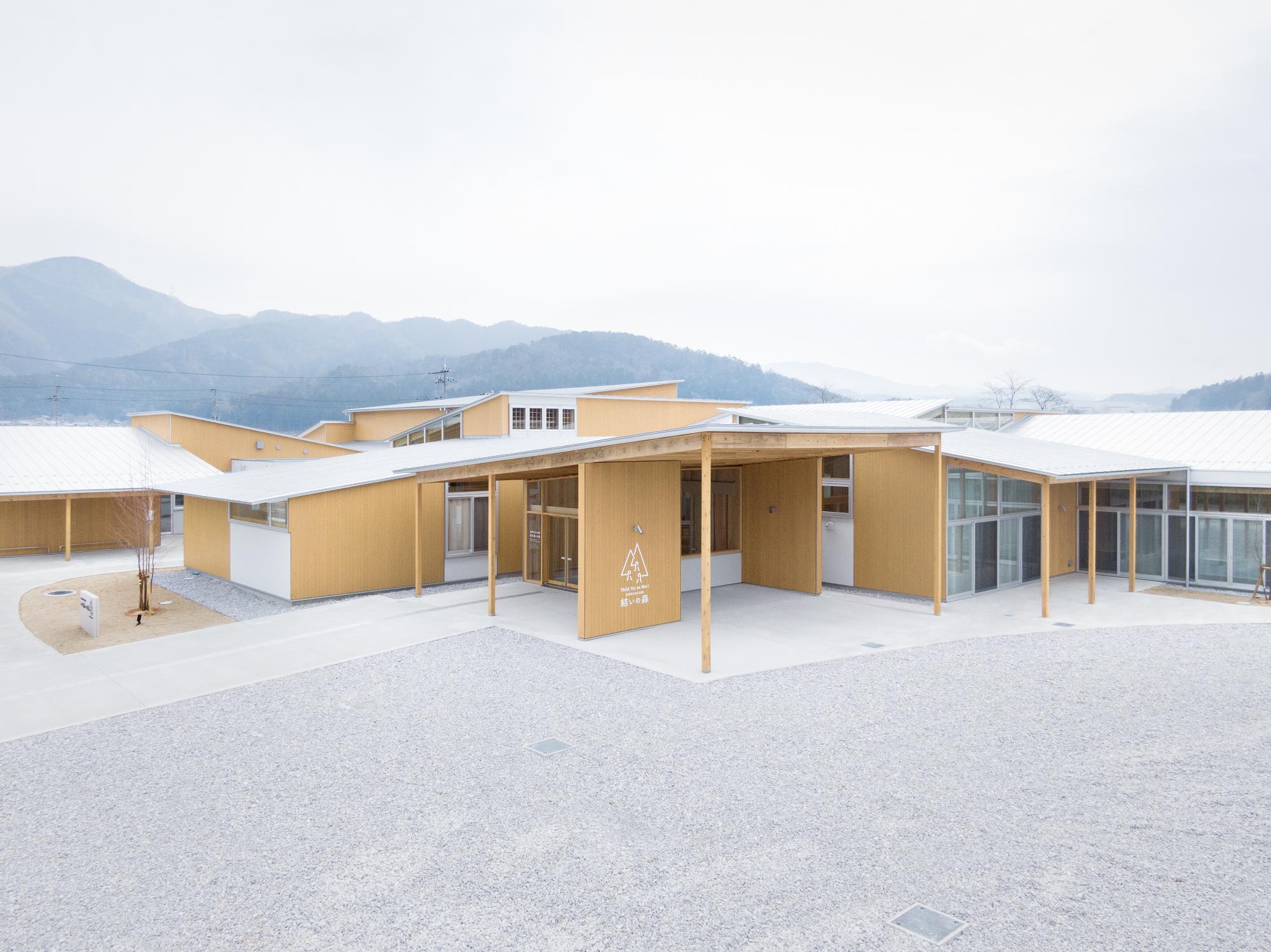 山々に囲まれた敷地に建つ木造平屋建築の外観全体を写した写真