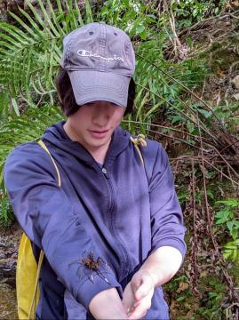 帽子をかぶった男性の右腕に足の長い虫が乗っている写真