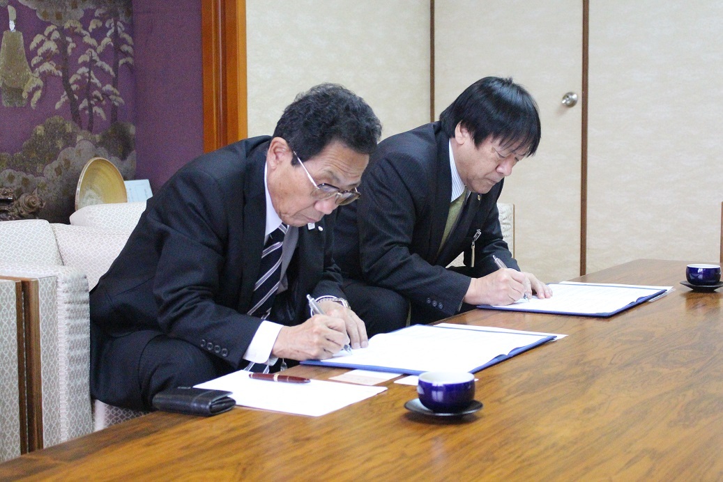 スーツ姿の2人の男性が各々書類にサインを行っている写真