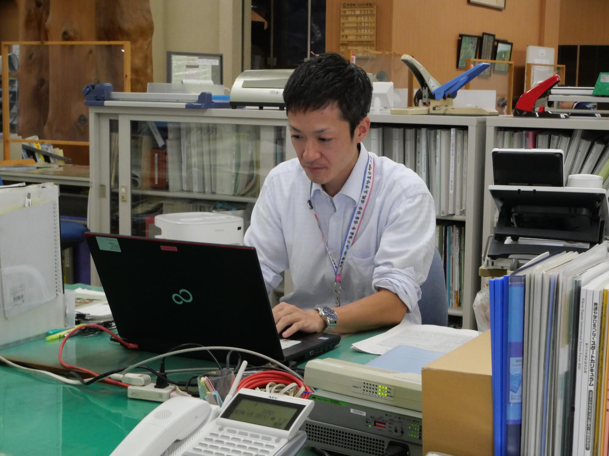 ワイシャツ姿の男性がデスクでノートパソコンを見ている写真