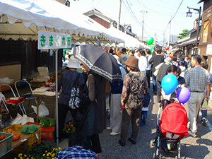 屋外に設置されたテントの屋根の下にお店ができていて人々が集まっている写真